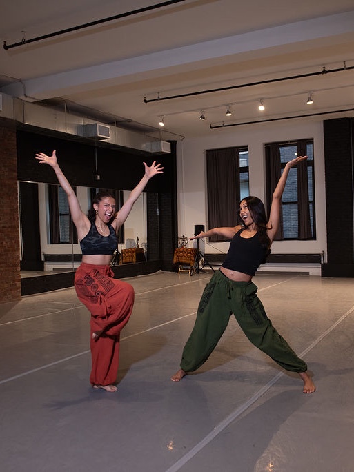 Shivani and a fellow dancer mid-celebration, arms flung wide, in a sunlit dance studio